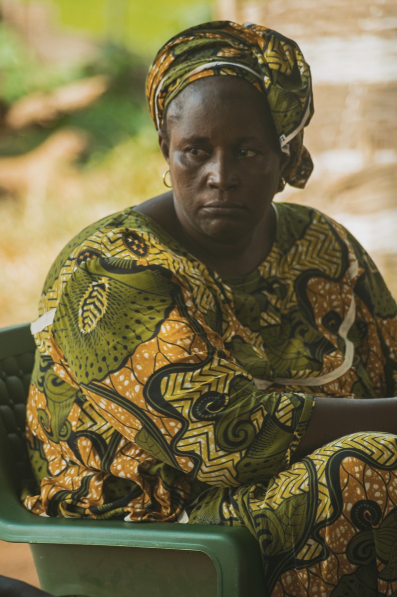 Portrait d’une femme assise, vêtue d’un boubou à motifs verts et orange et d’un foulard